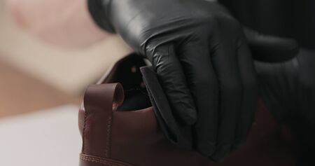 man hands in black gloves applying protective cream to brown leather sneakers, wide photoの写真素材