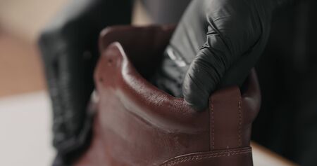 man hands in black gloves applying protective cream to brown leather sneakers, wide photo