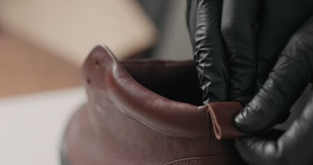 man hands in black gloves applying protective cream to brown leather sneakers, wide photo