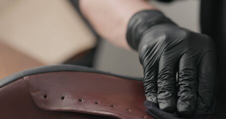 man hands in black gloves applying protective cream to brown leather sneakers, wide photoの写真素材