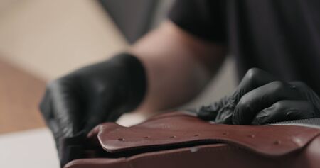 man hands in black gloves applying protective cream to brown leather sneakers, wide photoの写真素材