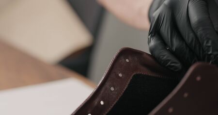 man hands in black gloves applying protective cream to brown leather sneakers, wide photo