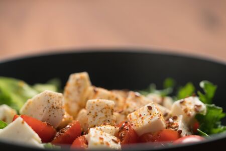 Healthy light salad with cherry tomatoes, mozzarella and frisee in black bowl on walnut surface...