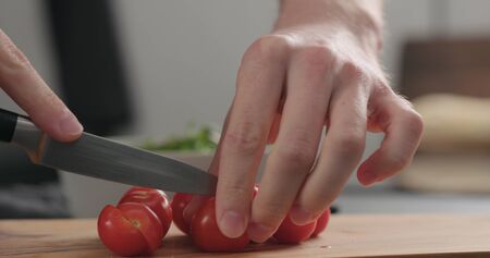 closeup man cutting cherry tomatoes on olive boardの写真素材