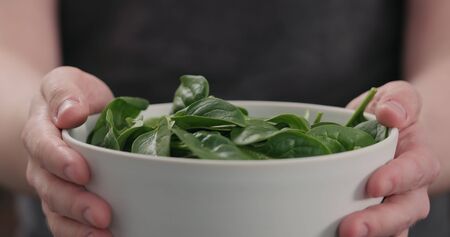 man show fresh spinach leaves in white bowl closeup, wide photo