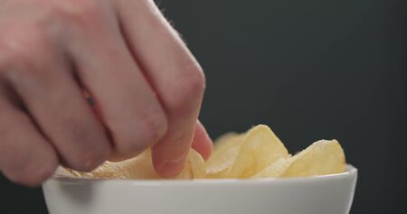 man hand take potato chips in white bowl on black background closeup, wide photo