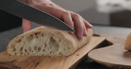 man slicing ciabatta with bread knife on olive board, wide photo