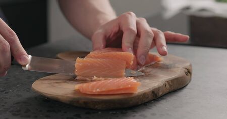 man hands slicing salted trout with knife on olive wood boardの写真素材