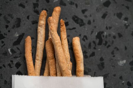 Traditional italian snack - grissini in white paper bag on concrete surface