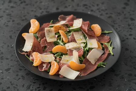 Salad with prosciutto, tangerines and vintage cheese on black plateの写真素材