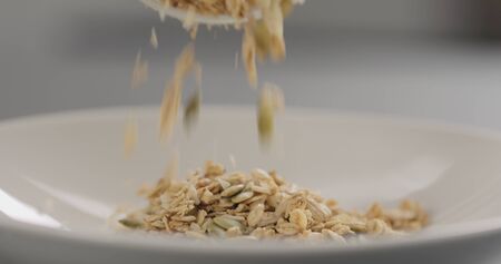 granola with almond flakes and pumpkin seeds fall into white bowl closeup, wide photoの写真素材