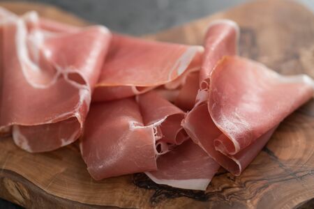 Thin italian prosciutto slices on olive wood board on conctere background , shallow focusの写真素材