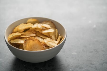 Potato chip slightly sprinkled with black pepper in white bowl on concrete background with copy space, shallow focusの写真素材