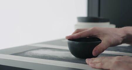 man hands sand bottom of black ceramic bowl, wide photoの写真素材