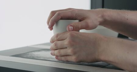 man hands sand bottom of white ceramic glass, wide photo