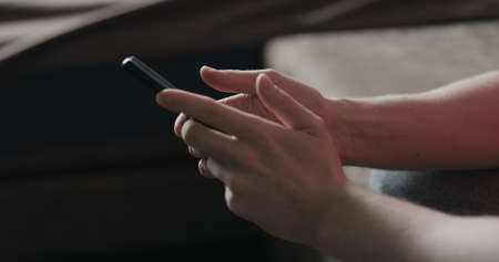 Closeup young man in black t-shirt typing messages on smartphone working from home side view