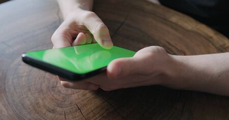 Closeup young man use smartphone with green screen while sitting at the table, wide photo