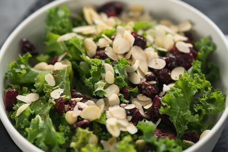 Salad with kale, cranberries and almond flakes in white bowl on linen napkin, shallow focusの写真素材