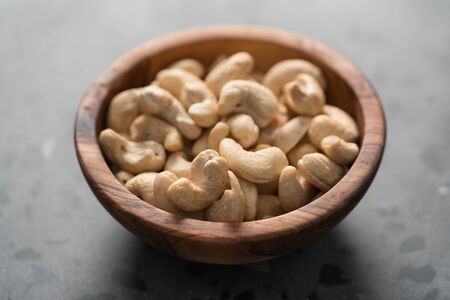 Dry cashew nuts in wood olive bowl on concrete background closeup, shallow focusの写真素材