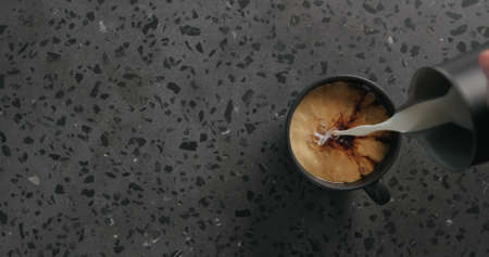 pour cream into black coffee in black cup on concrete background top viewの写真素材