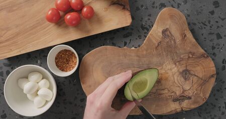 Top view man hands slice half of ripe avocado on concrete countertop, wide photo