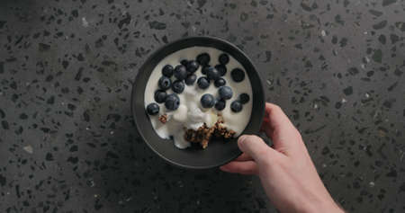 top view man hands put chocolate granola, almond flakes and blueberry in black bowl on terrazzo surfaceの写真素材