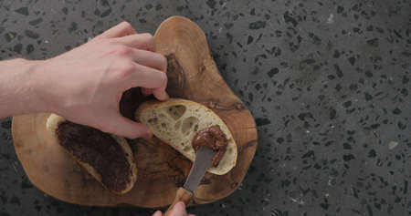 man spreading chocolate spread on ciabatta slice on olive board top view