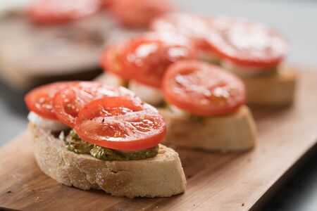 Bruschetta with tomatoes, mozzarella and pesto on olive wood board, shallow focus