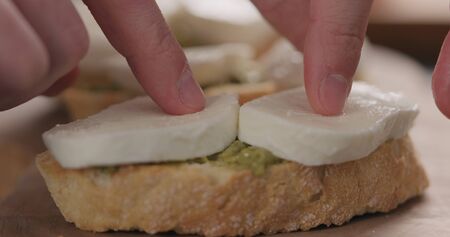 man put mozzarella slices on ciabatta slice with pesto on olive board, wide photo