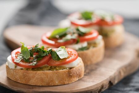 Bruschetta with mozzarella, tomatoes and basil with pesto on olive wood boardの写真素材