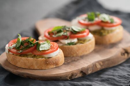 Bruschetta with mozzarella, tomatoes and basil with pesto on olive wood boardの写真素材