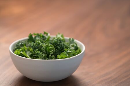 kale salad leaves in white bowl on walnut table with copy space, shallow focusの写真素材