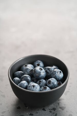 Ripe blueberries in black bowl on concrete background with copy spaceの写真素材