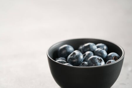 Ripe blueberries in black bowl on concrete background with copy spaceの写真素材