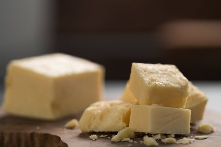 White cheddar cheese pieces on olive wood board, shallow focus