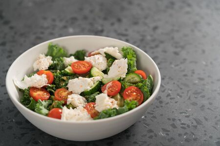 Salad with kale, tomatoes, cucumbers and mozzarella in white bowl, shallow focusの写真素材