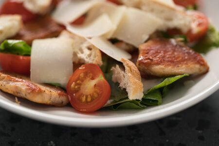 Fresh caesar salad with chicken and cherry tomatoes in white bowl, shallow focus