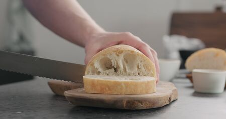 man slicing ciabatta bread on olive wood boardの写真素材