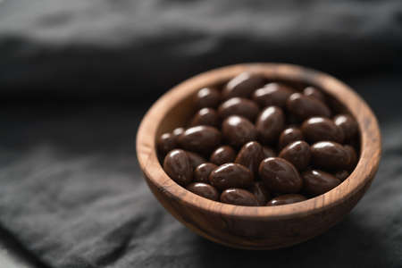 Milk chocolate dragee in olive wood bowl on linen background, shallow focusの写真素材
