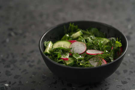 Summer fresh salad with radish, cucumber and herbs in black bowl, shallow focusの写真素材