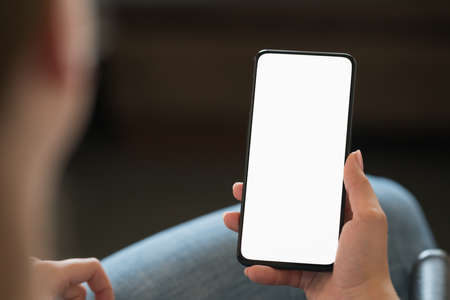 Young woman sitting in chair with modern smartphone with white screen, shallow focus