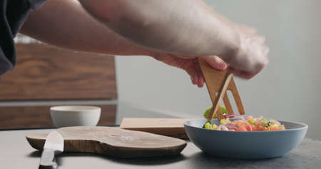 Man mixing greek salad in blue bowl with wood servers, wide photo
