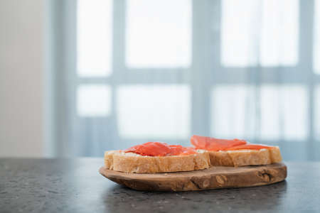 Sandwich with smoked salmon and cream cheese on olive woob board on kitchen countertop, shallow...