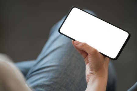Young woman hold smarphone with white screen while sitting in a chair, shallow focus