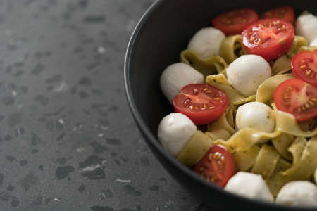fettuccine pasta with pesto, mozzarella and cherry tomatoes in black bowl on concrete background closeup with copy spaceの写真素材