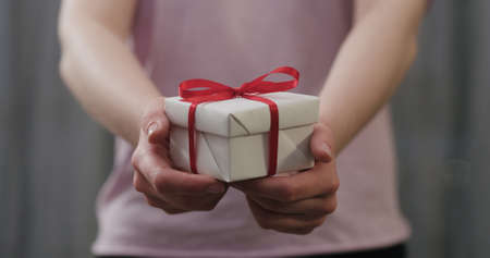 young woman stand and show white gift box with red ribbon bow