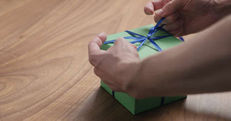 man hand tyingblue ribbon on green paper gift box on walnut table with copy spaceの写真素材