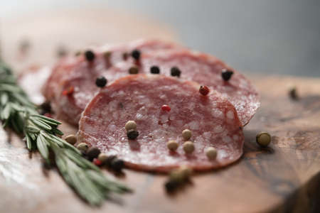 Sliced salame milano sausage on olive wood board with rosemary and pepperの写真素材