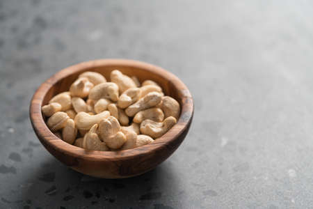 Dry cashew nuts in wood olive bowl on concrete background with copy spaceの写真素材