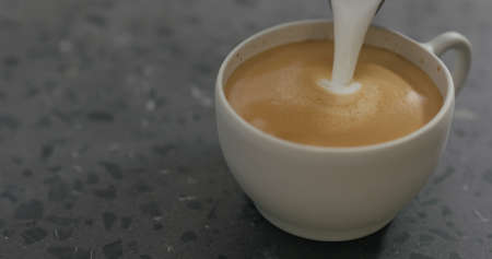 pouring steamed milk into cappuccino in white cup on terrazzo countertopの写真素材